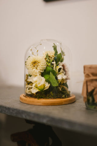 a glass dome with flowers and leaves on a table
